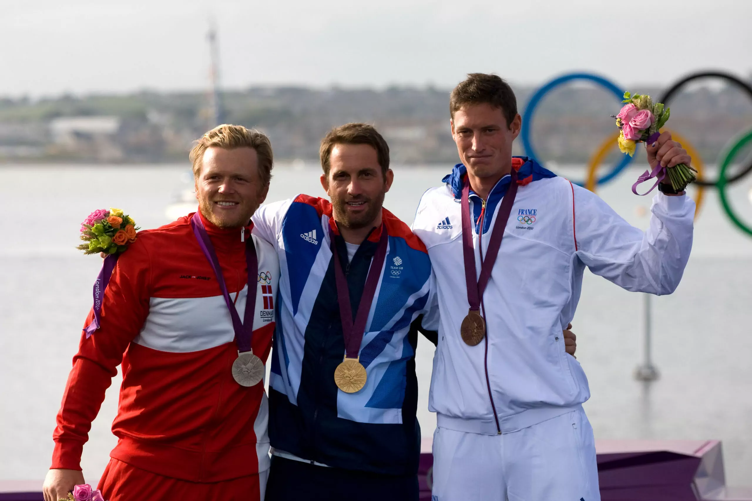 Olympic sailing medalists standing together on the London 2012 podium, symbolizing shared success and respect