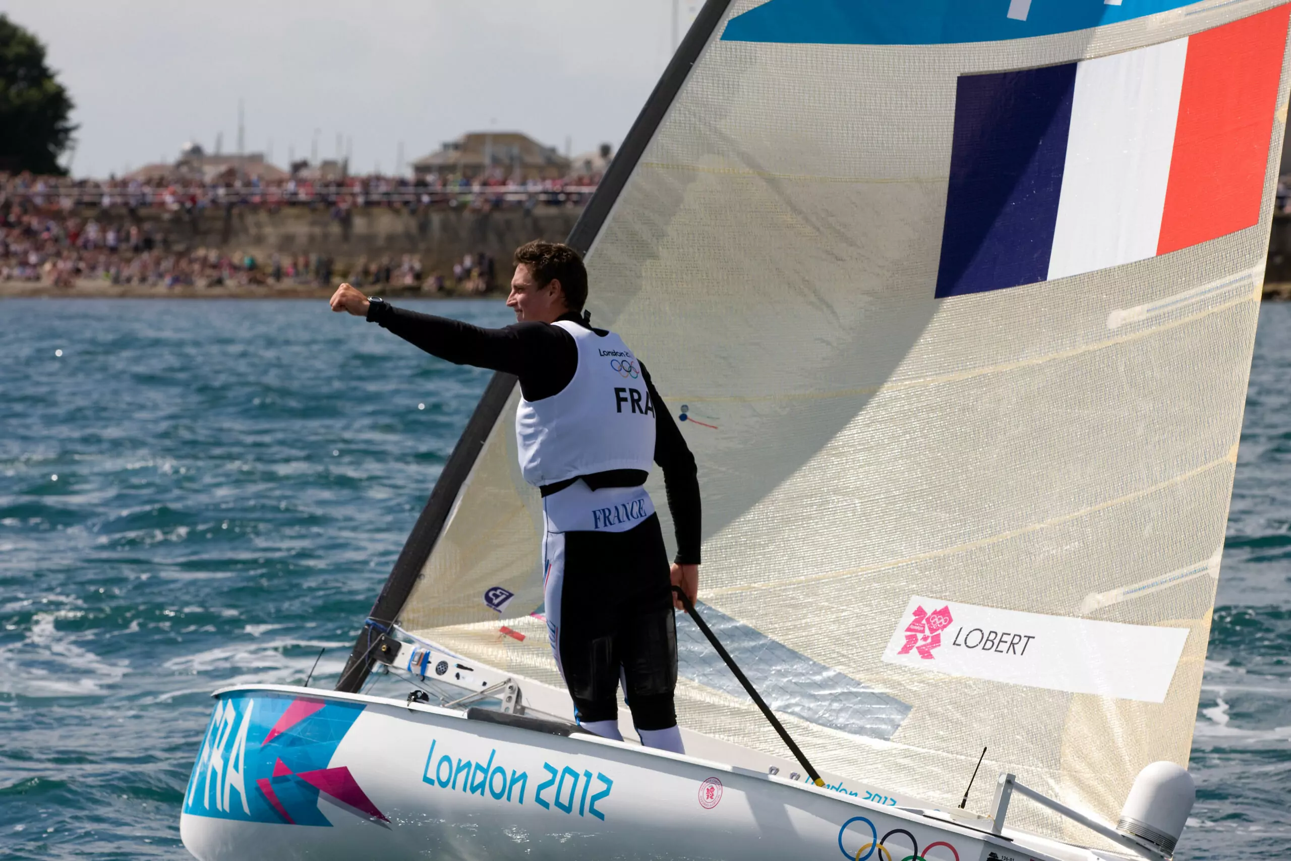 Jonathan Lobert raising his fist after a sailing race at the London 2012 Olympics, symbolizing triumph and determination
