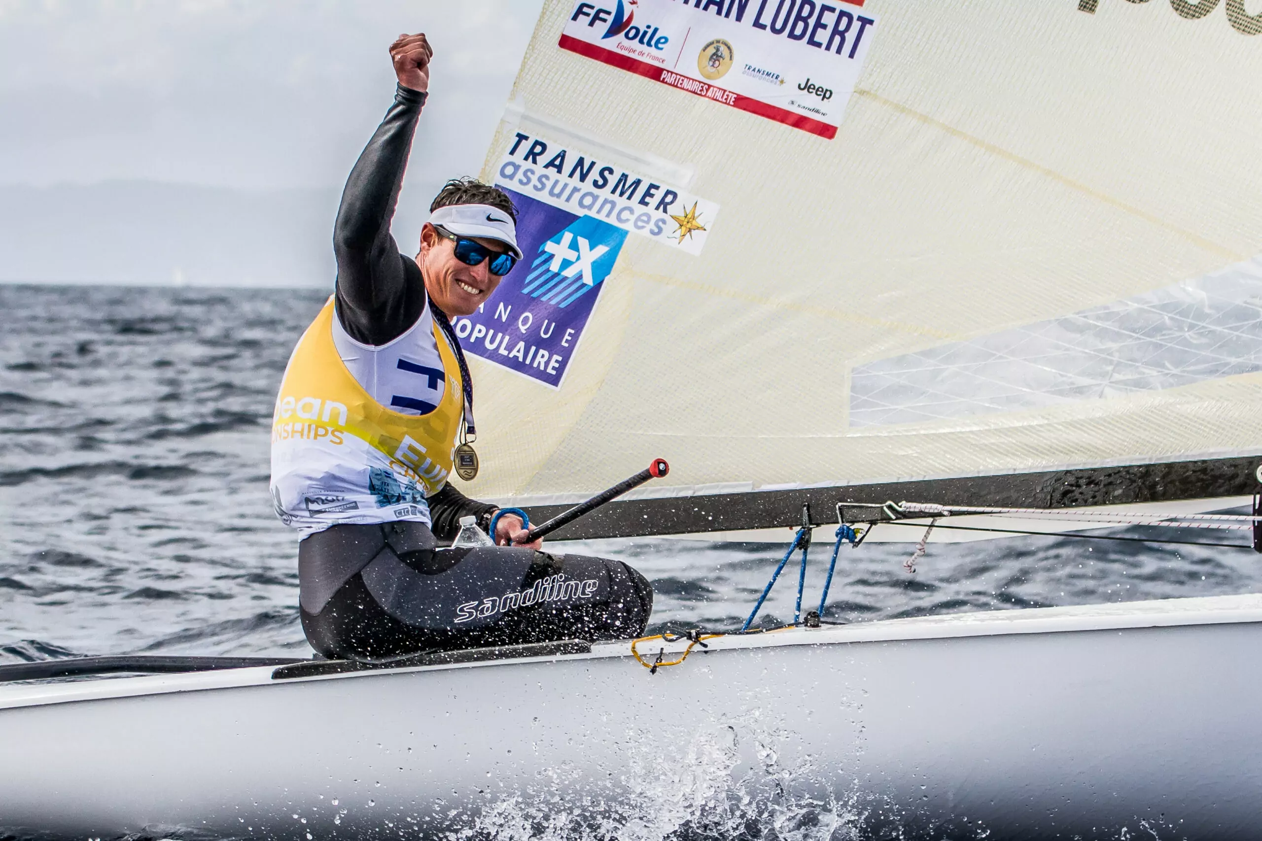 Jonathan Lobert lève le poing après sa victoire au Championnat d’Europe de voile, symbole de réussite et de détermination